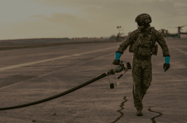 Soldier carrying a fuel line across a tarmac at an airfield