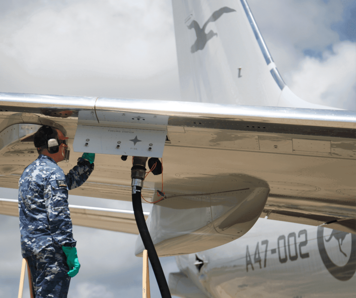 Technician monitors a fuel hose connected to the wing of an aircraft
