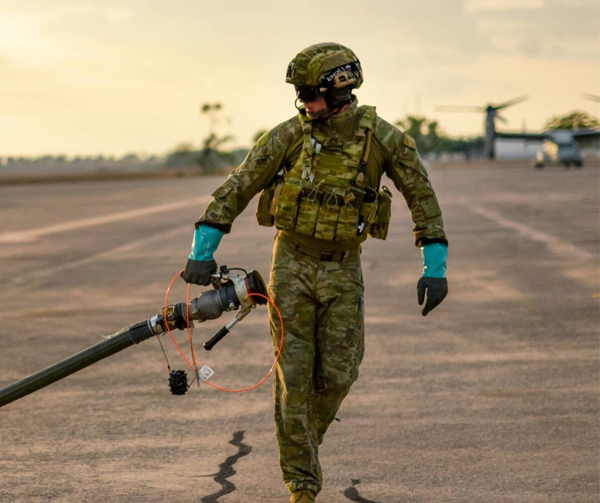 Soldier carrying a fuel line across a tarmac at an airfield
